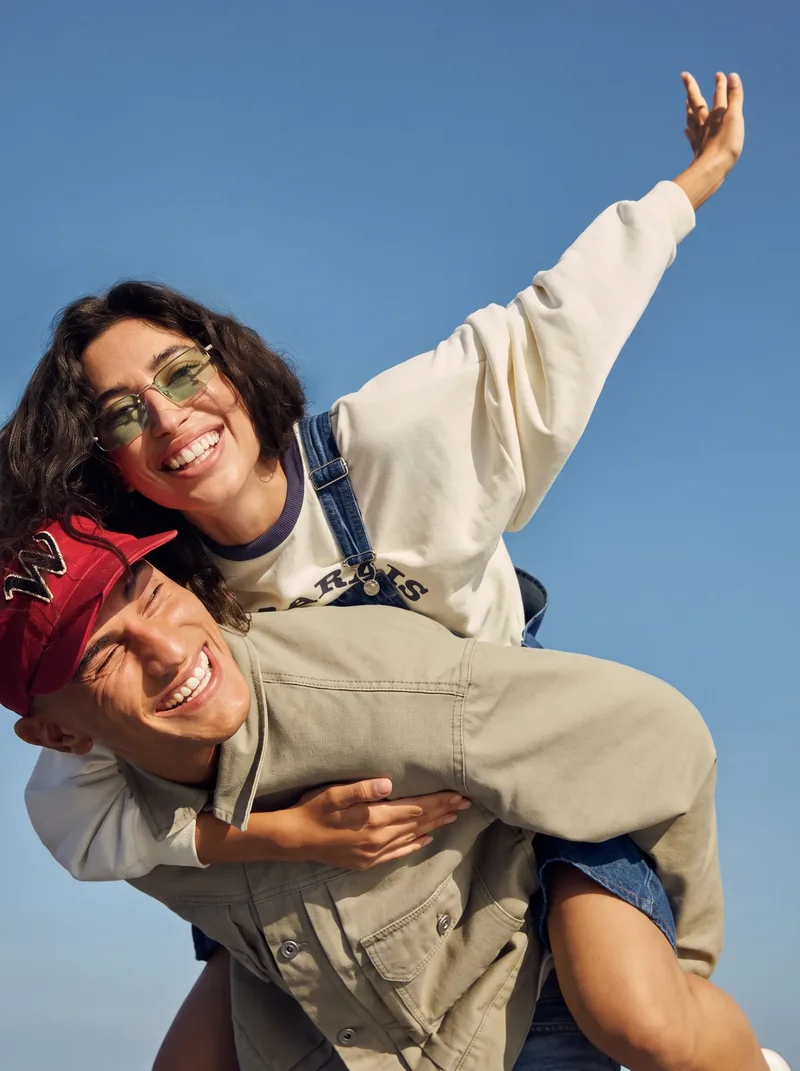 Two friends laughing, one carried on the other's back under a blue sky